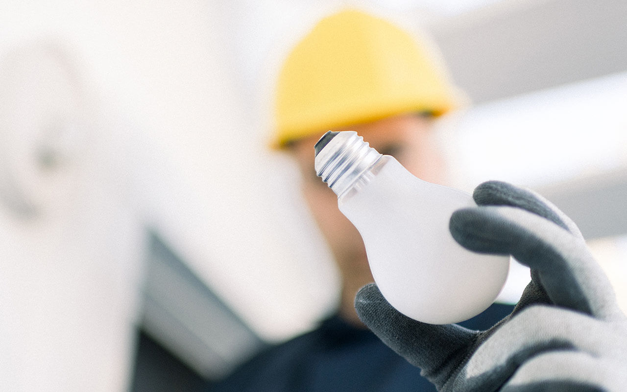 closeup of an electrician with yellow hard hat holding a lightbulb